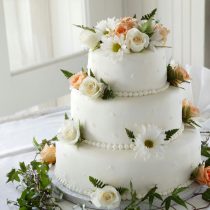 Elegant white wedding cake adorned with fresh roses and daisies, perfect for a romantic celebration.