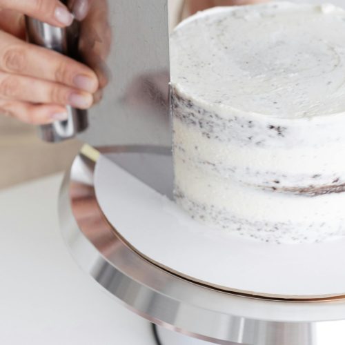 Crop unrecognizable confectioner standing at table while making delicious cake placed on white table in light kitchen